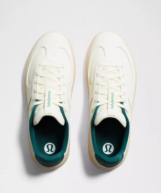 White sneakers with green soles on a light gray background