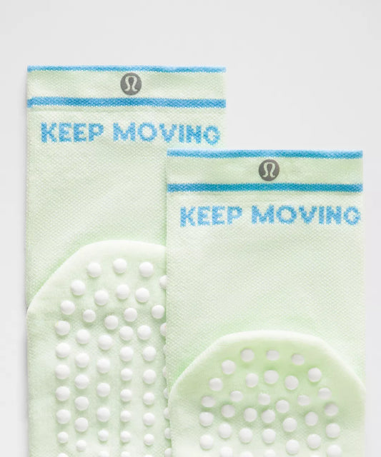 Two green socks with 'KEEP MOVING' text and brand logo on a light gray background