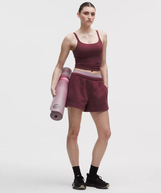 Woman in maroon athletic outfit holding a pink yoga mat on a white background