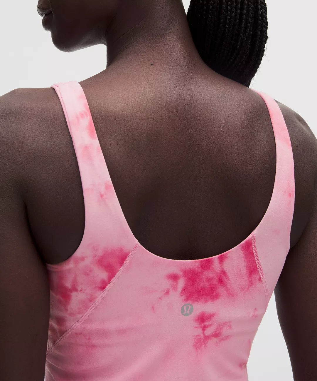Person wearing a pink tie-dye tank top with a brand logo on a plain background