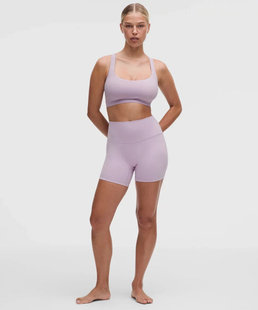 Woman wearing a lavender sports bra and shorts set on a white background