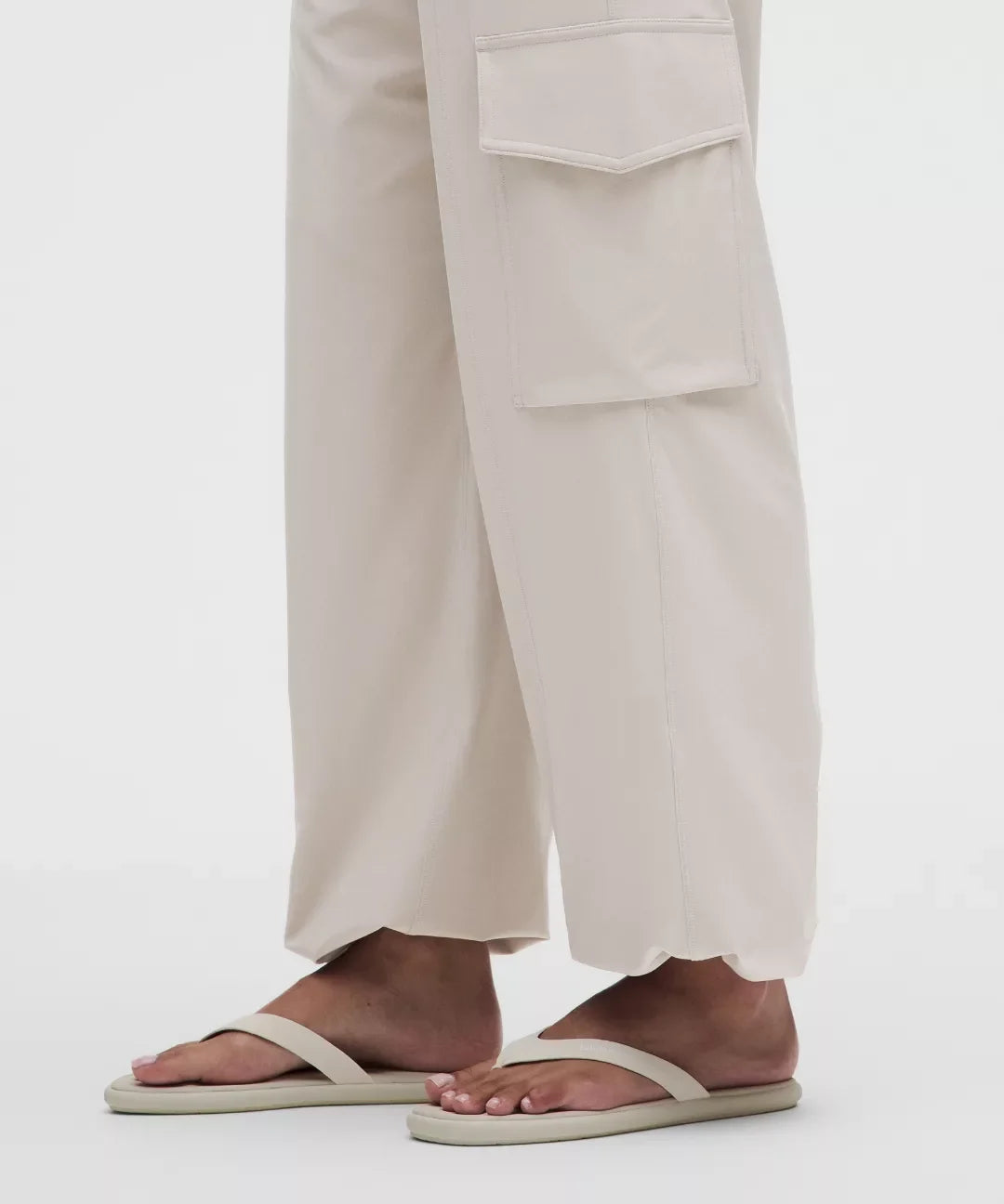Person wearing beige sandals and light-colored pants on a white background