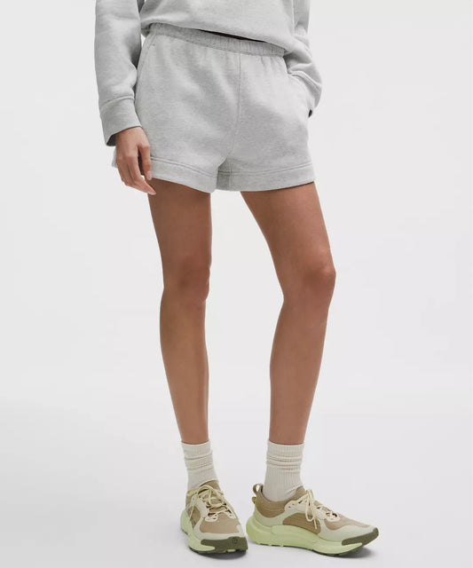 Person wearing gray sweatshirt and shorts with beige sneakers on a white background