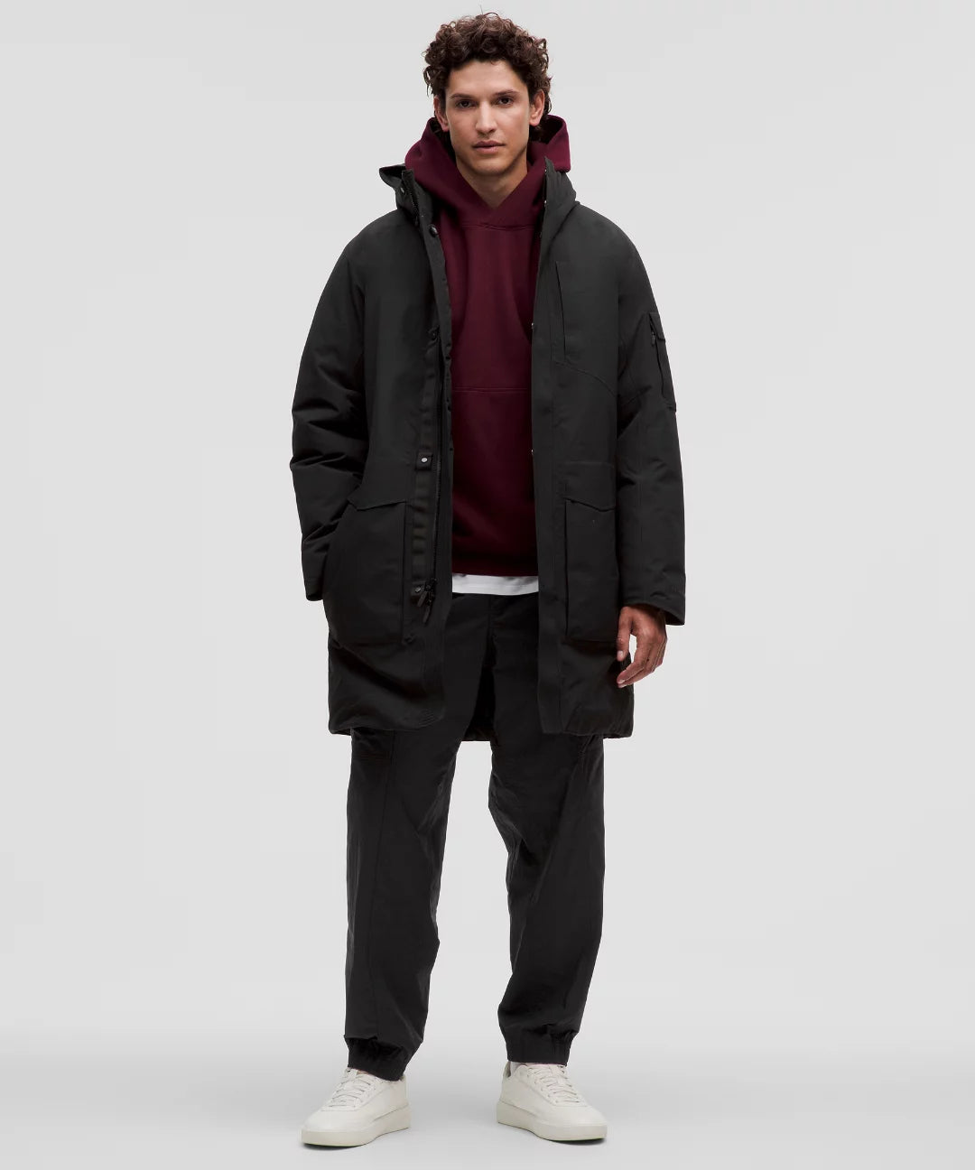 Man wearing a black coat over a red hoodie on a white background