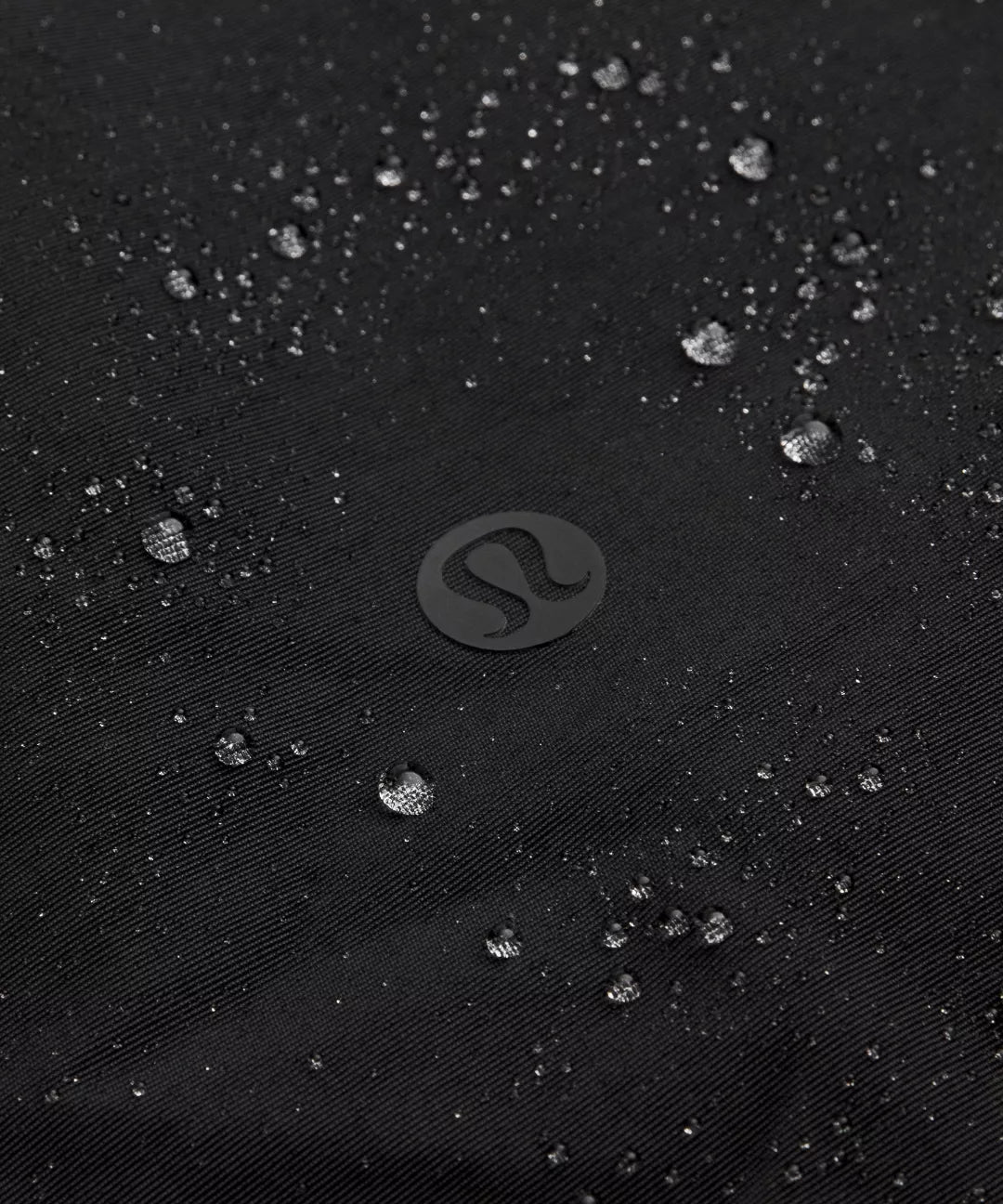 Close-up of water droplets on a black textured surface with a brand logo.