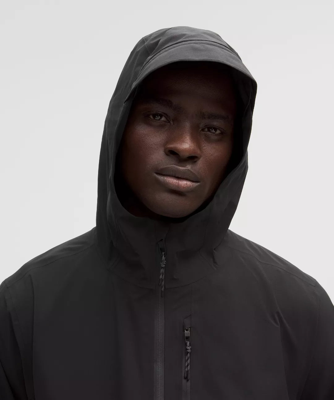 Person wearing a black hooded jacket against a plain background