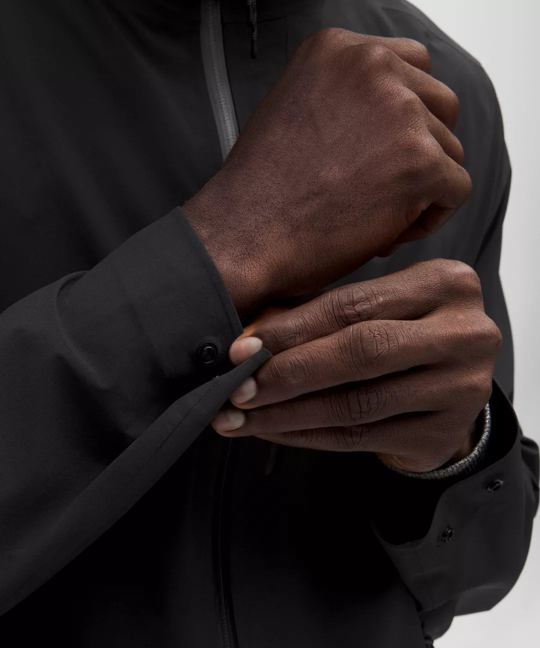 Person wearing a black jacket with hands adjusting the hood against a white background