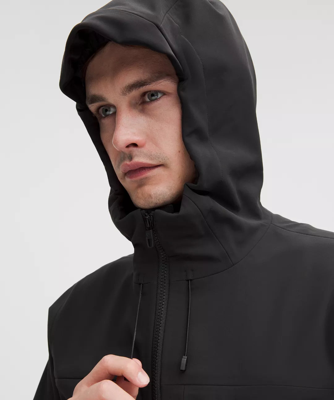 Man wearing a black hooded jacket on a light gray background