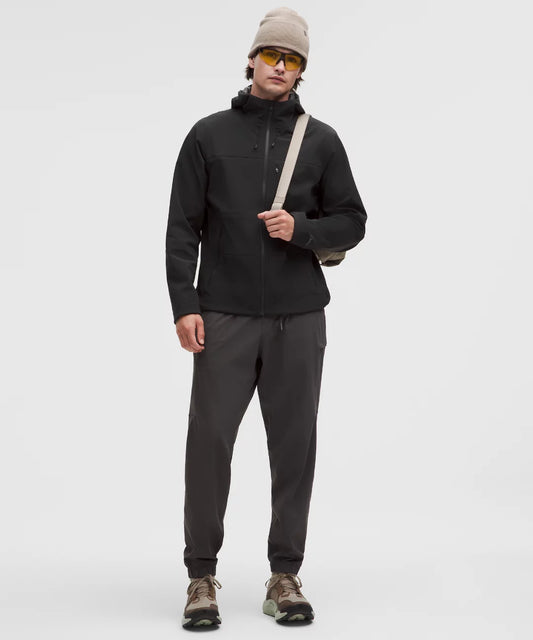 Person wearing a black jacket, gray pants, and a beige beanie on a white background