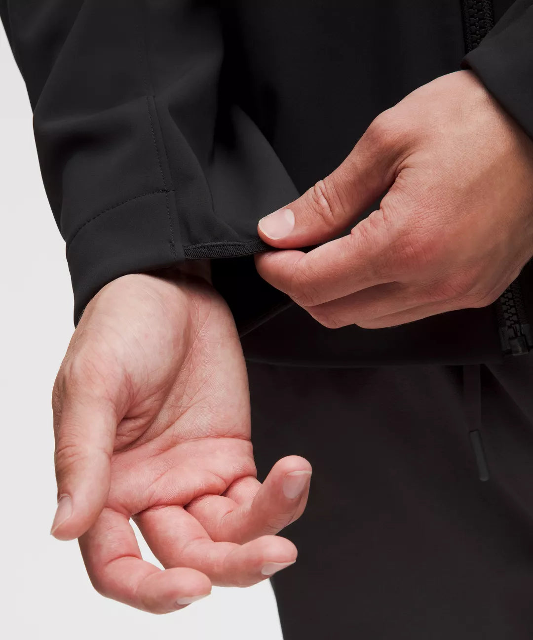 Close-up of hands adjusting a black jacket on a light gray background