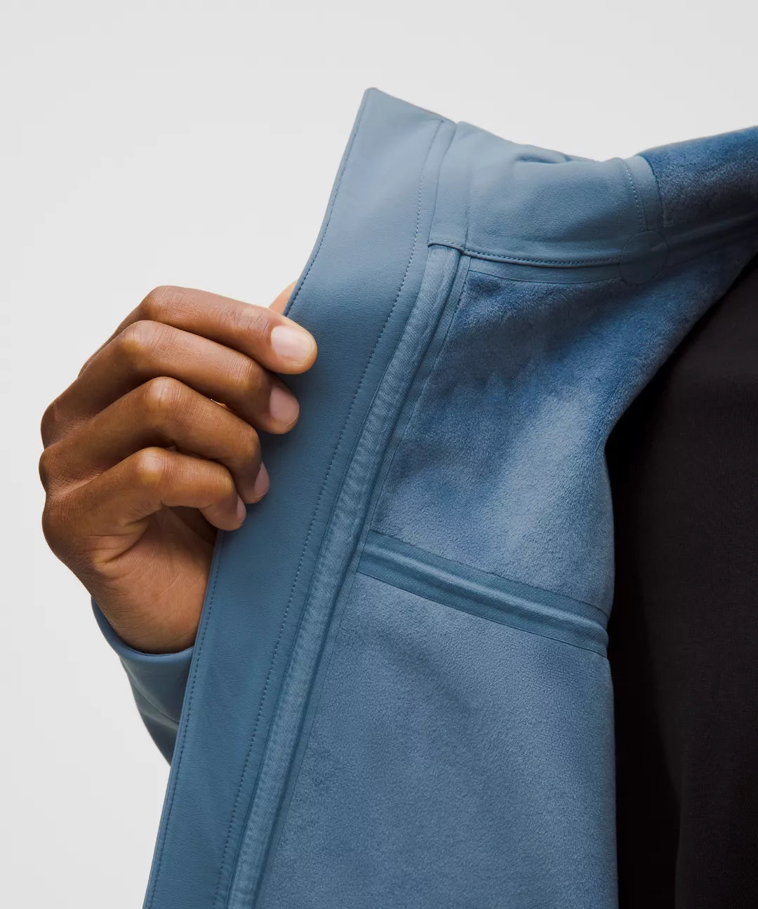 Hand zipping a blue jacket against a neutral background