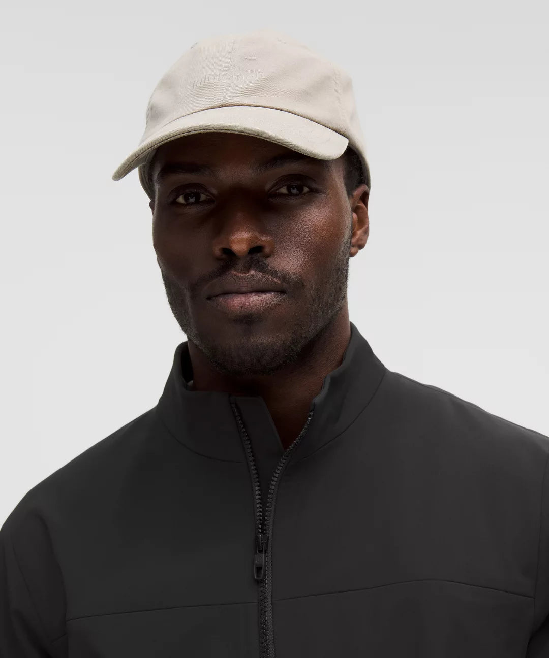 Man wearing a beige cap and black jacket against a gray background