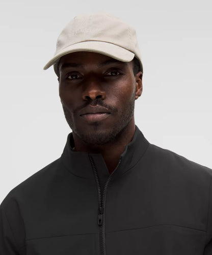 Man wearing a beige cap and black jacket against a gray background