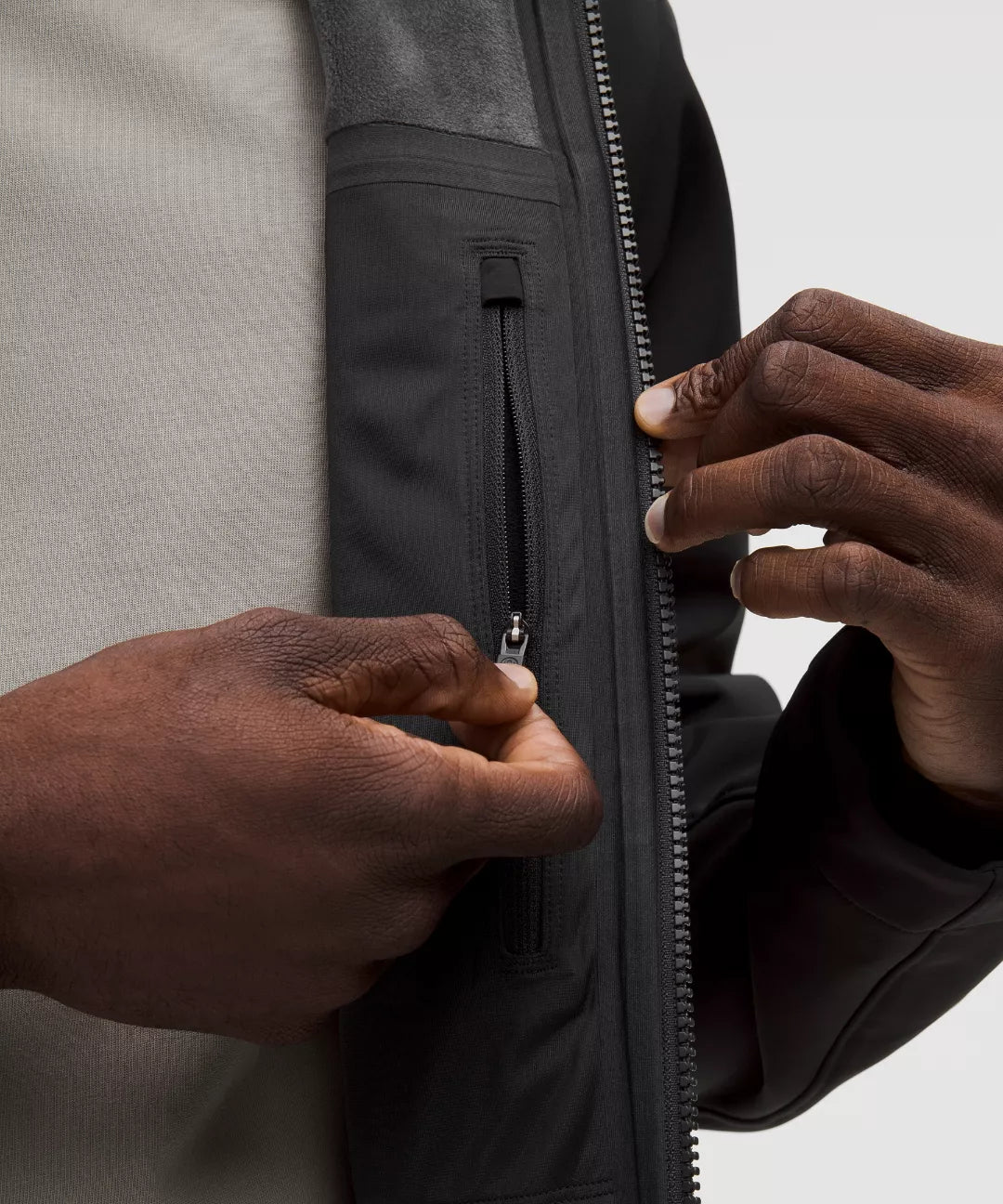 Person zipping up a black jacket with a neutral background