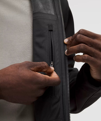 Person zipping up a black jacket with a neutral background