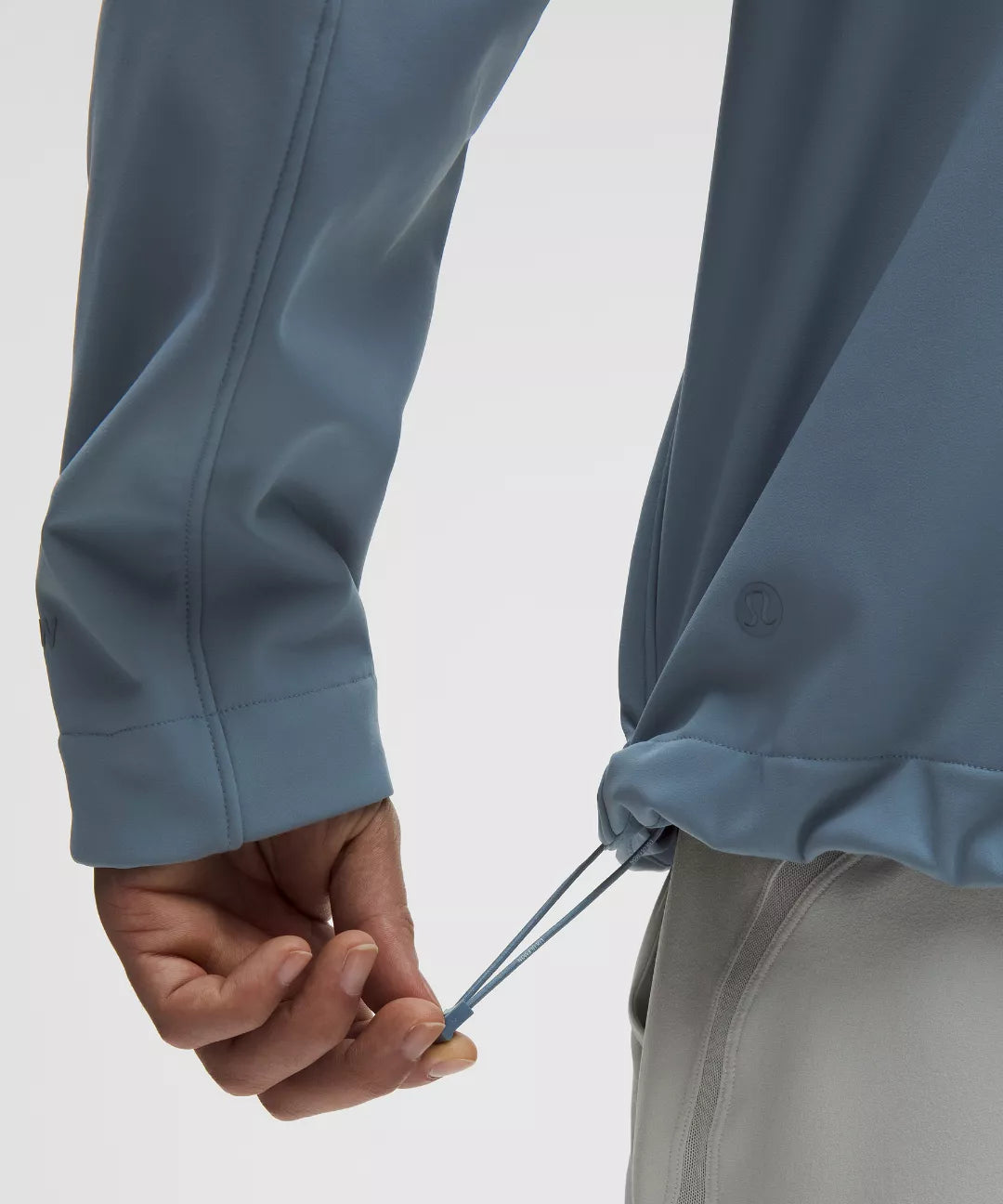 Close-up of a person adjusting the drawstring of a blue jacket on a white background