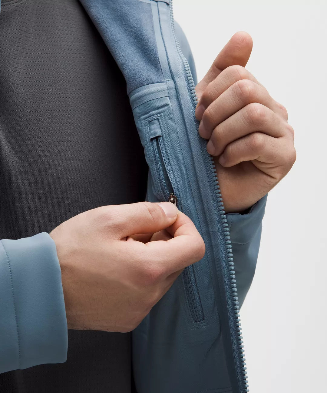 Person zipping up a blue jacket with a neutral background