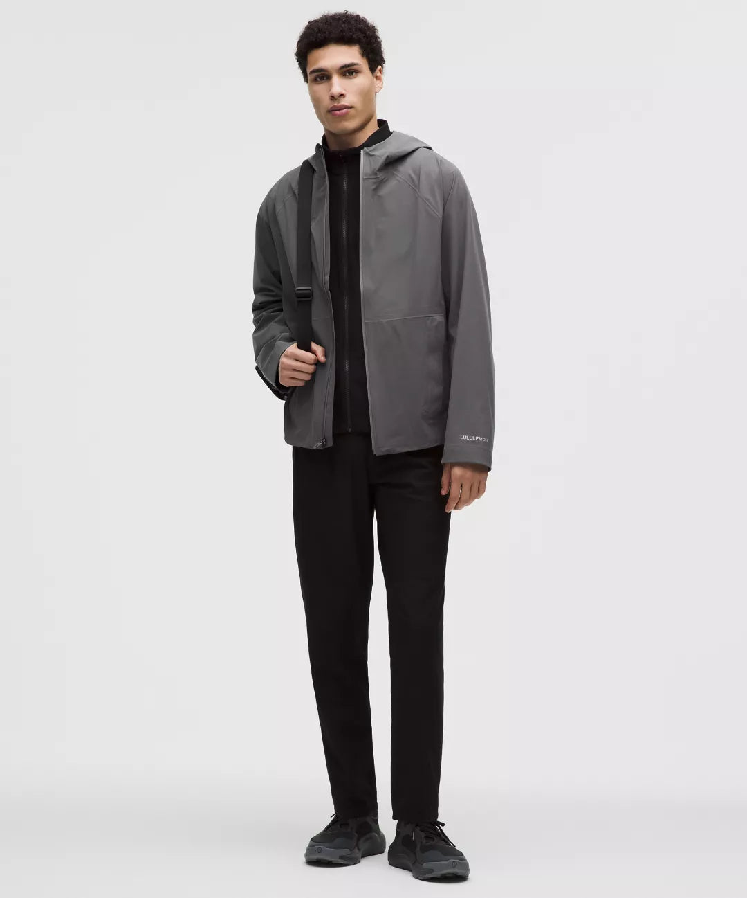 Man wearing a gray jacket over a black shirt and pants on a white background