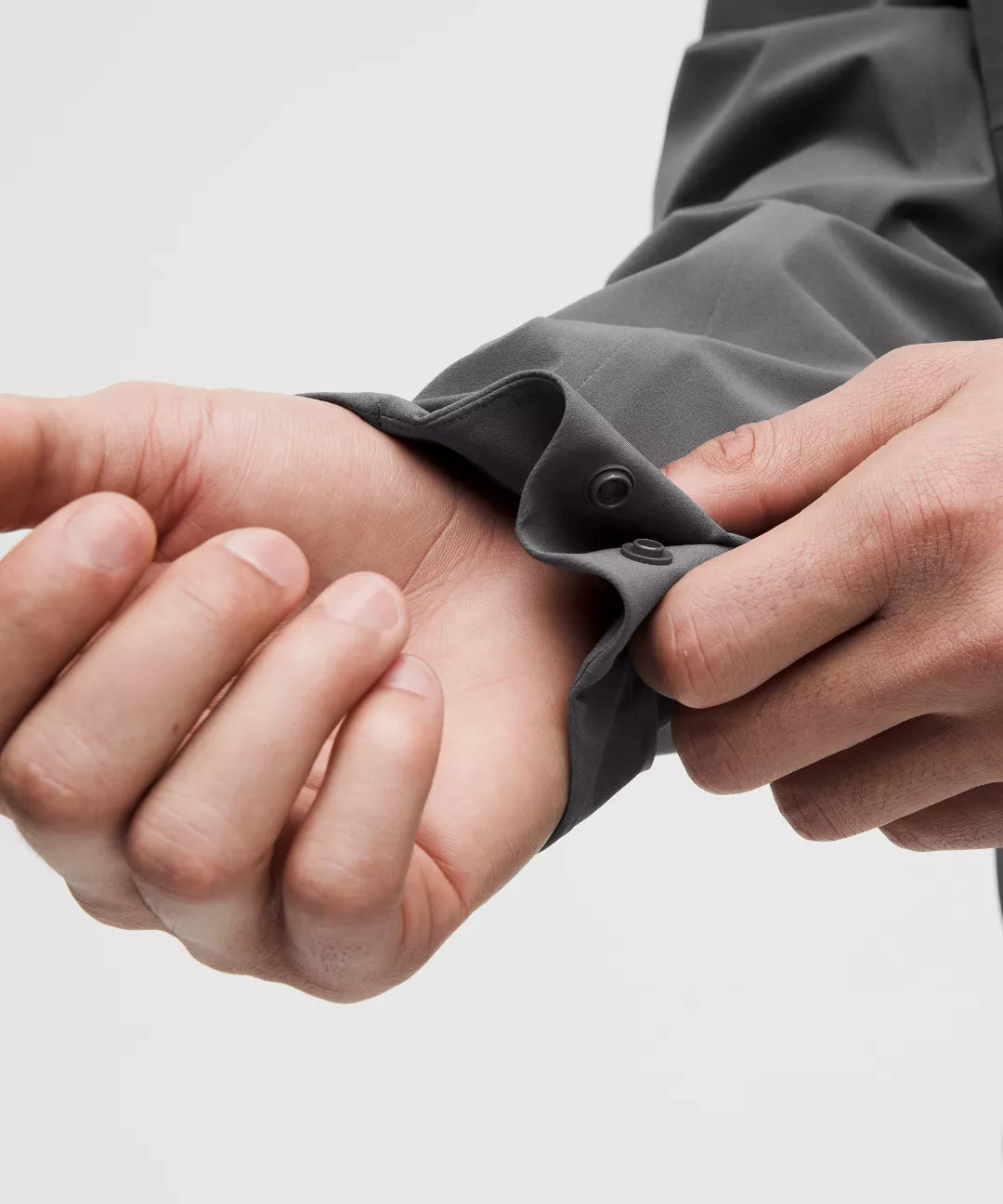 Person adjusting a gray sleeve with a button on a light gray background