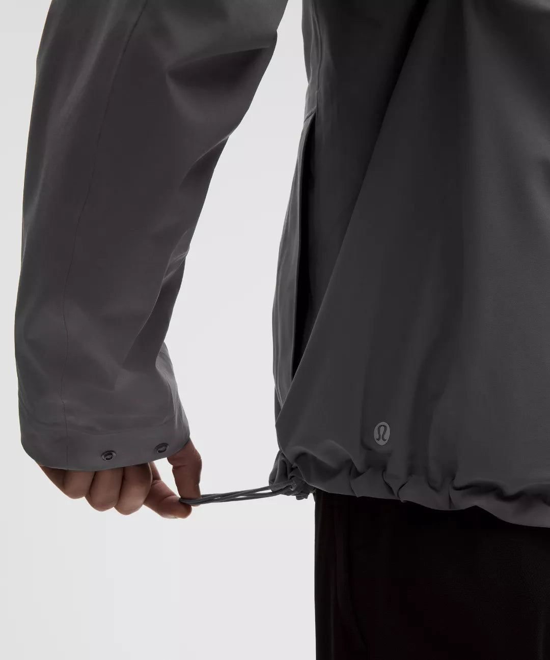 Person adjusting the hood of a black raincoat on a light gray background