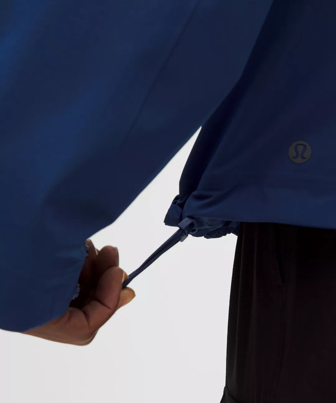 Person adjusting the hood of a blue jacket with a visible brand logo on a white background