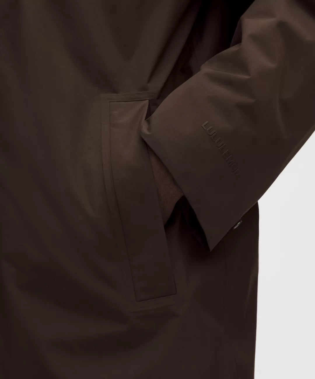 Close-up of a brown coat with a visible brand logo on a white background