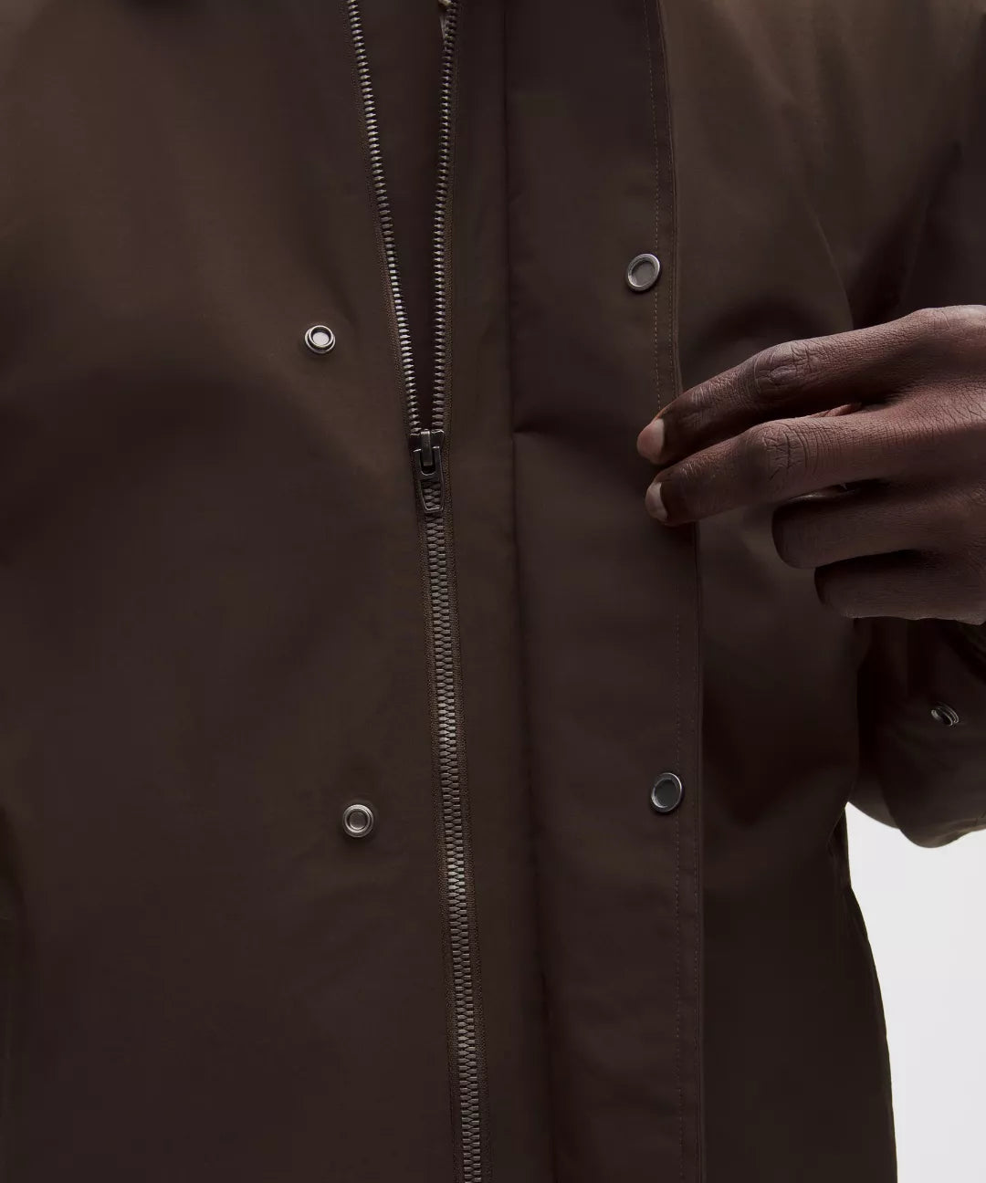 Close-up of a dark brown coat with a hand adjusting the zipper.