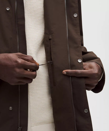 Close-up of a person wearing a brown coat with a white sweater underneath, on a plain background.