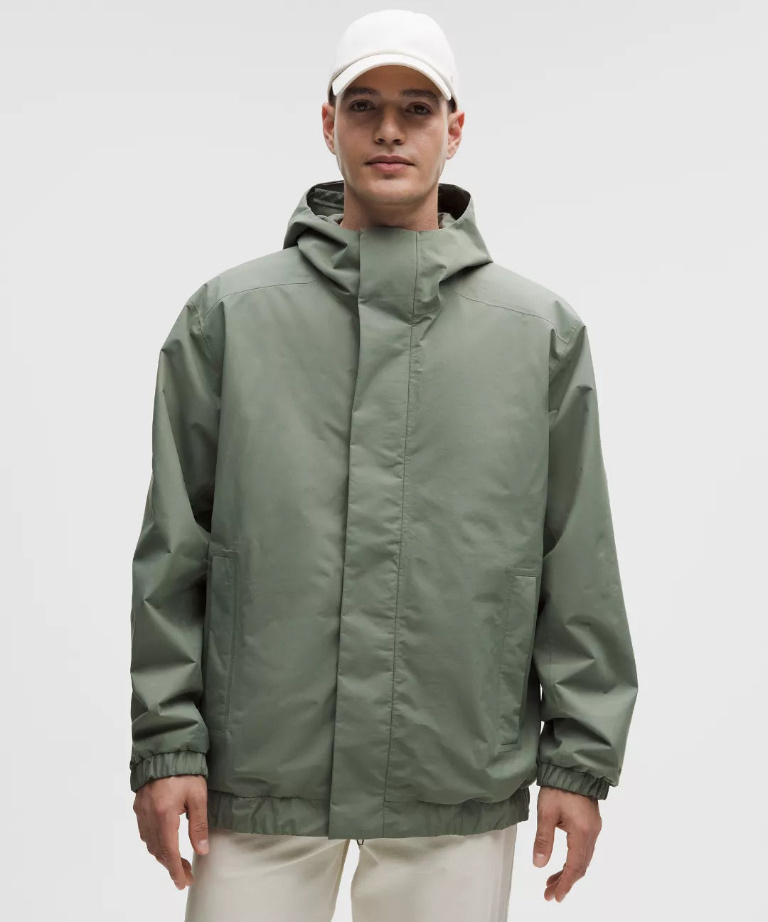 Person wearing a green raincoat and white cap on a gray background