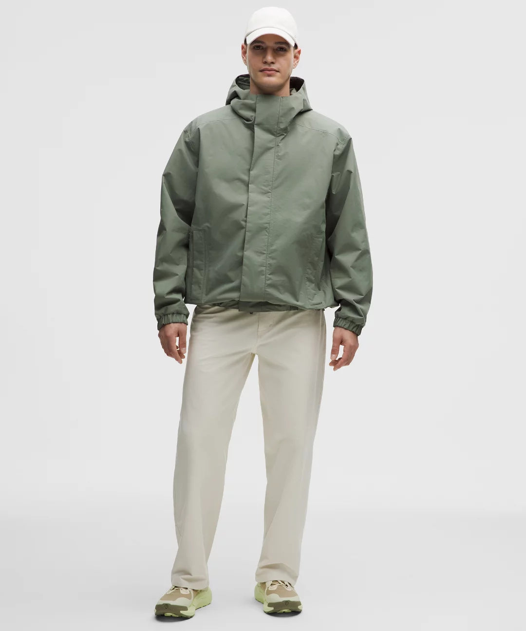 Man wearing a green raincoat and beige pants on a white background