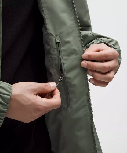 Person zipping up a green jacket with a neutral background