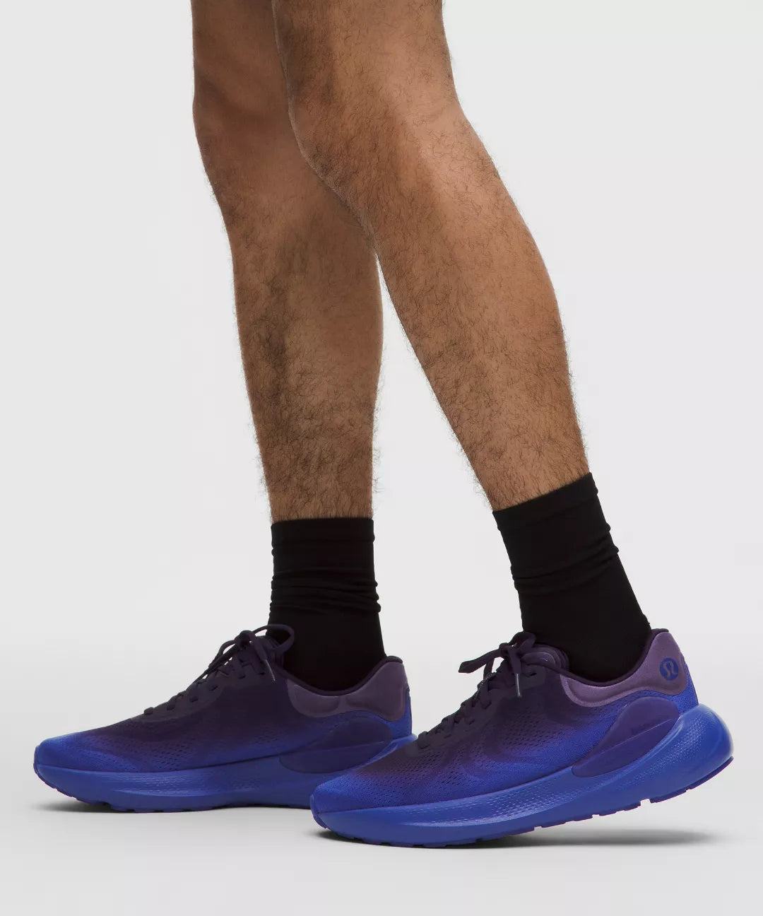 Blue athletic shoes worn with black socks on a light gray background