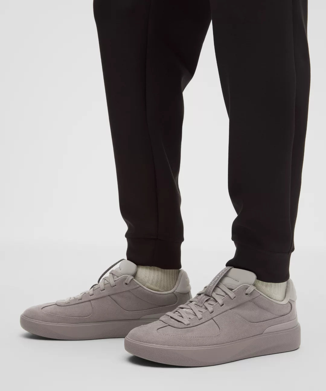Person wearing black jogger pants and light gray sneakers on a white background