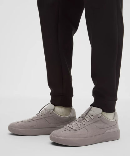 Person wearing black jogger pants and light gray sneakers on a white background