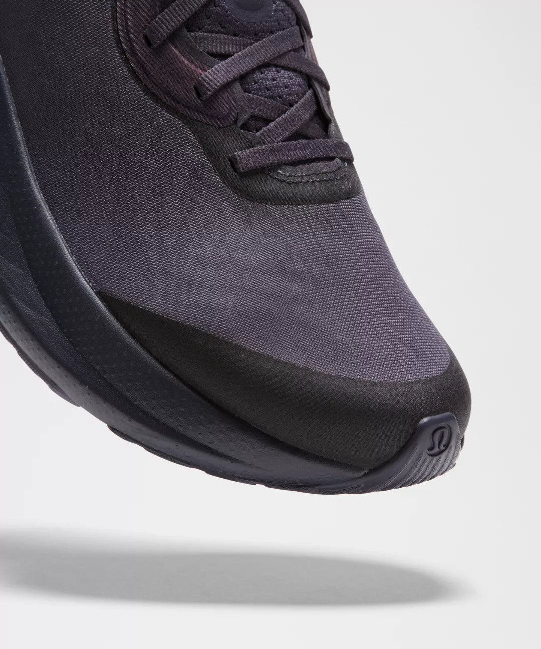 Close-up of a dark purple sneaker with a thick black sole on a light gray background