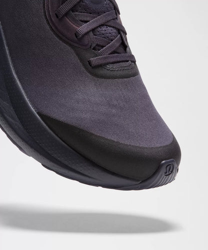 Close-up of a dark purple sneaker with a thick black sole on a light gray background