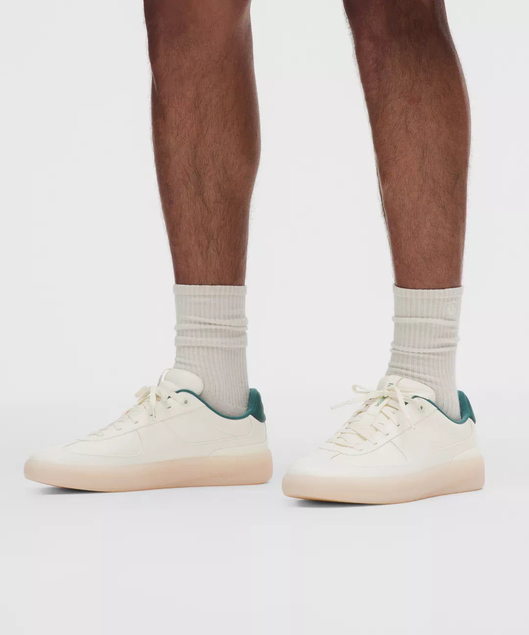 White sneakers with green accents worn by a person on a white background