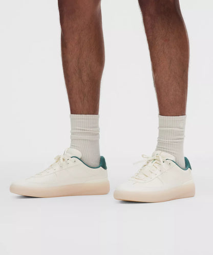 White sneakers with green accents worn by a person on a white background