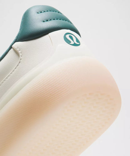 Close-up of a shoe with a green strap and visible brand logo on a light background