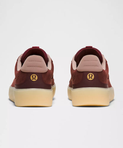 Maroon sneakers with a visible brand logo on a light gray background