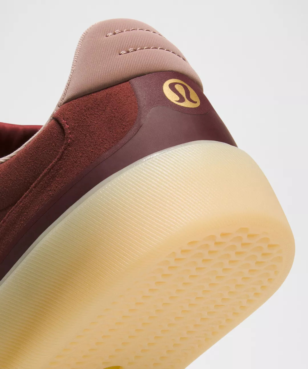 Close-up of a maroon sneaker with a yellow sole on a light gray background