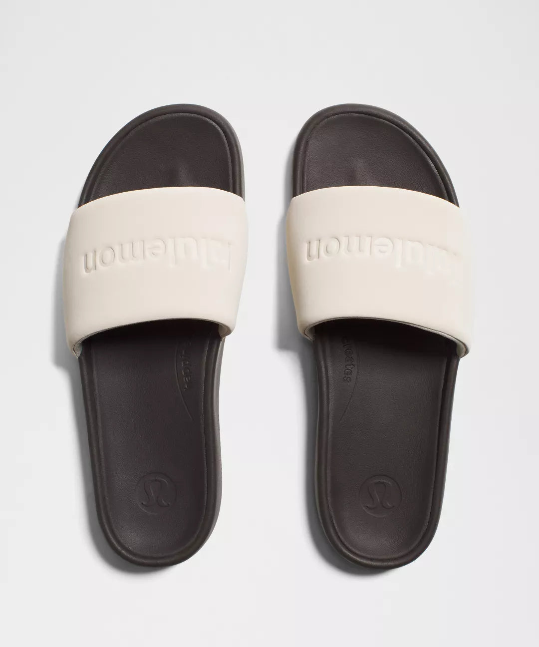 Pair of slides with white straps and black soles on a light gray background