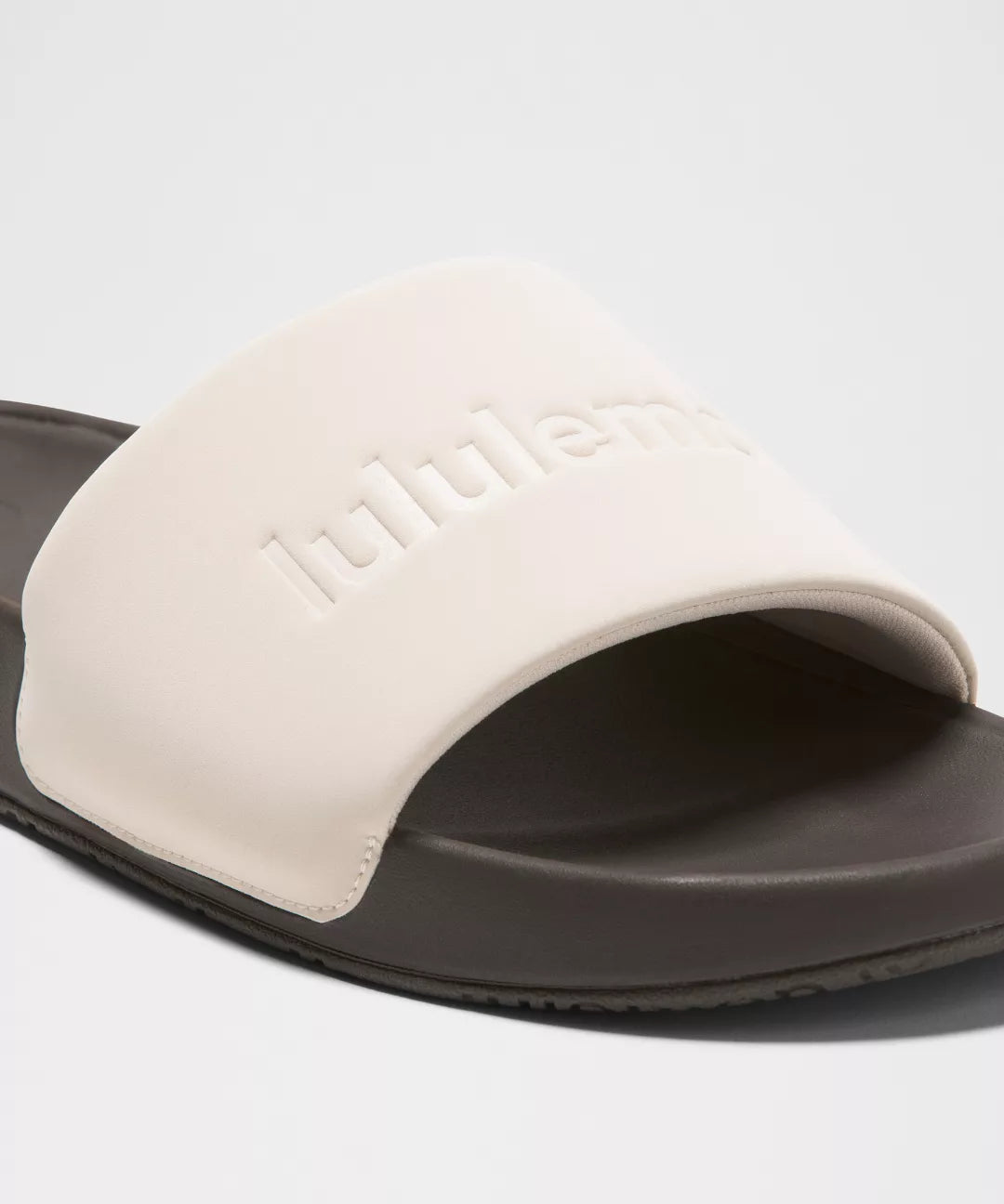 Slide sandal with beige strap and brown sole on a light gray background