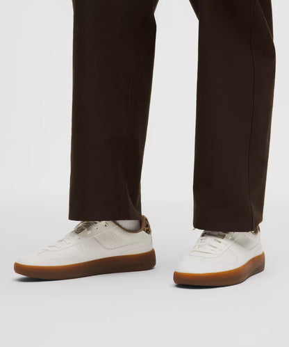 White sneakers with brown soles worn with dark pants on a white background
