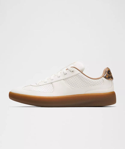 White sneaker with brown sole on a light gray background
