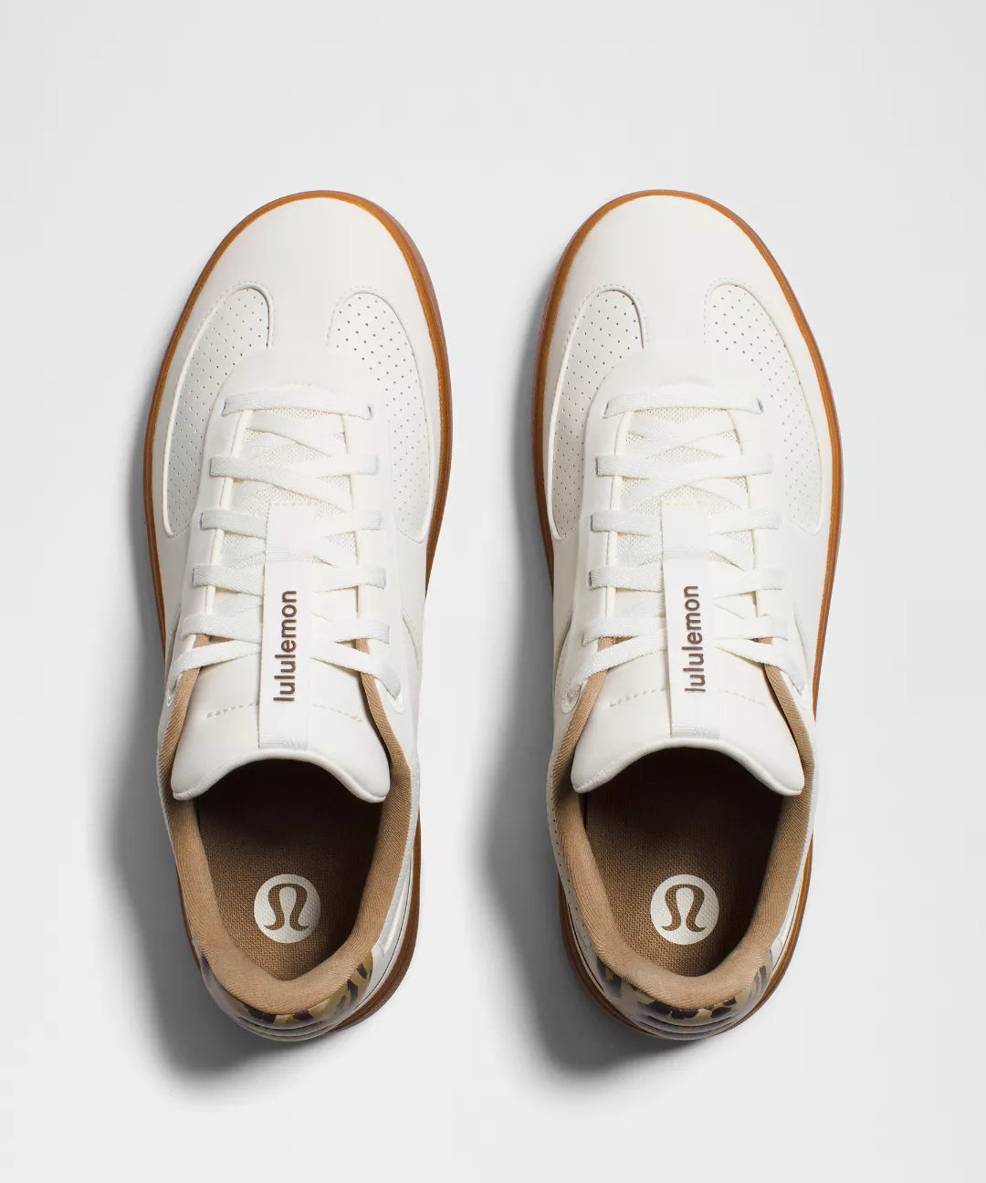 Pair of white sneakers with brown soles on a light gray background