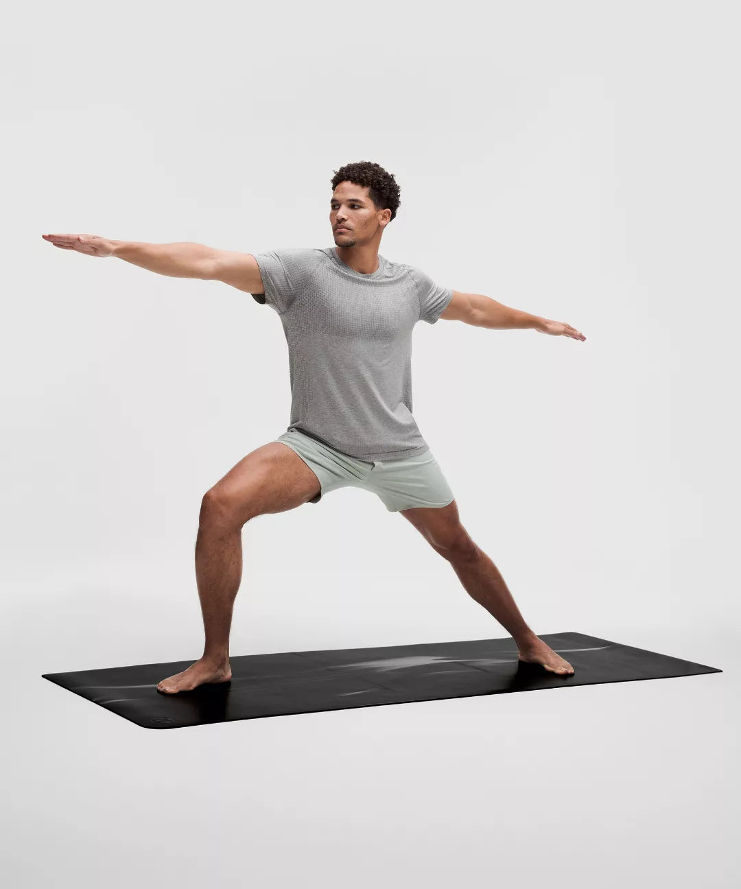 Man performing a yoga pose on a black mat with a plain background