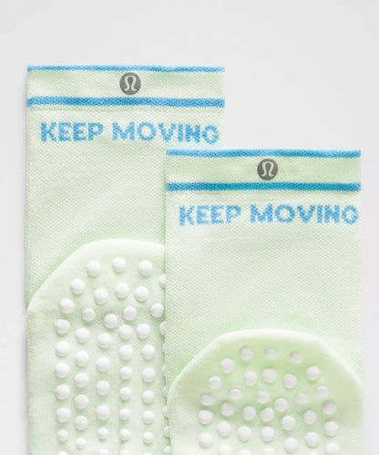 Two green socks with 'KEEP MOVING' text and brand logo on a light gray background