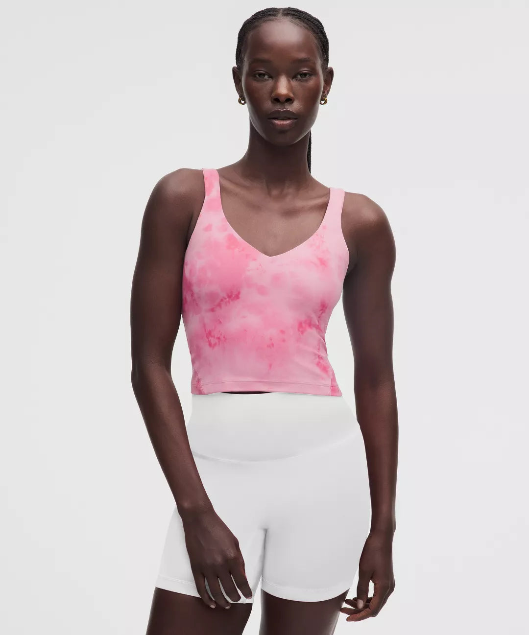 Woman wearing a pink tie-dye tank top and white shorts on a light gray background