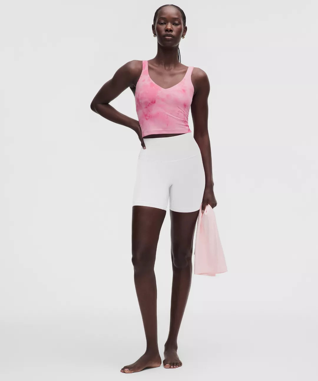 Woman wearing a pink tank top and white shorts holding a pink bag on a light gray background